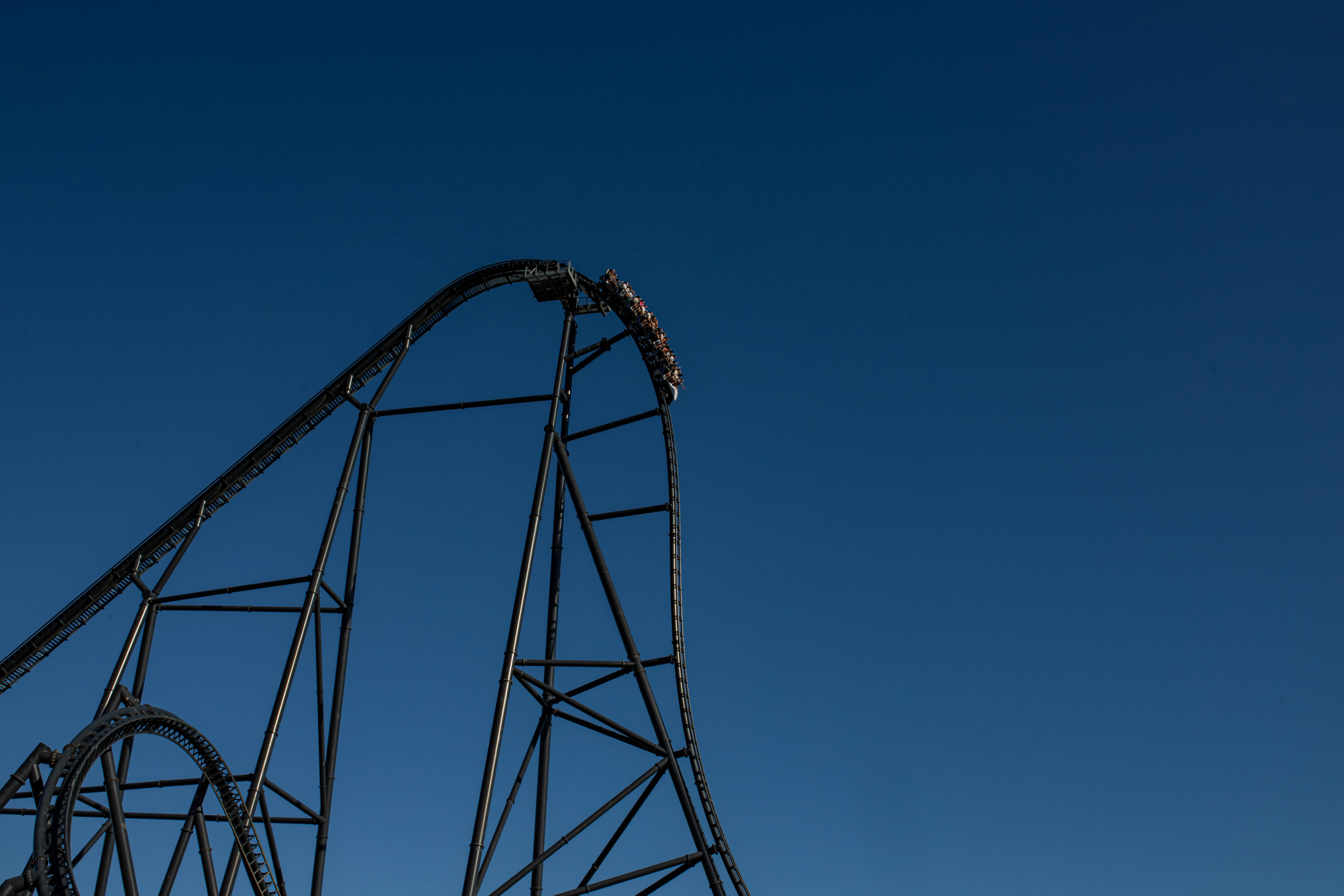 Big drop coaster skyline in Energylandia Tall black roller coaster hill with riders at the crest, dramatic skyline against deep blue sky.